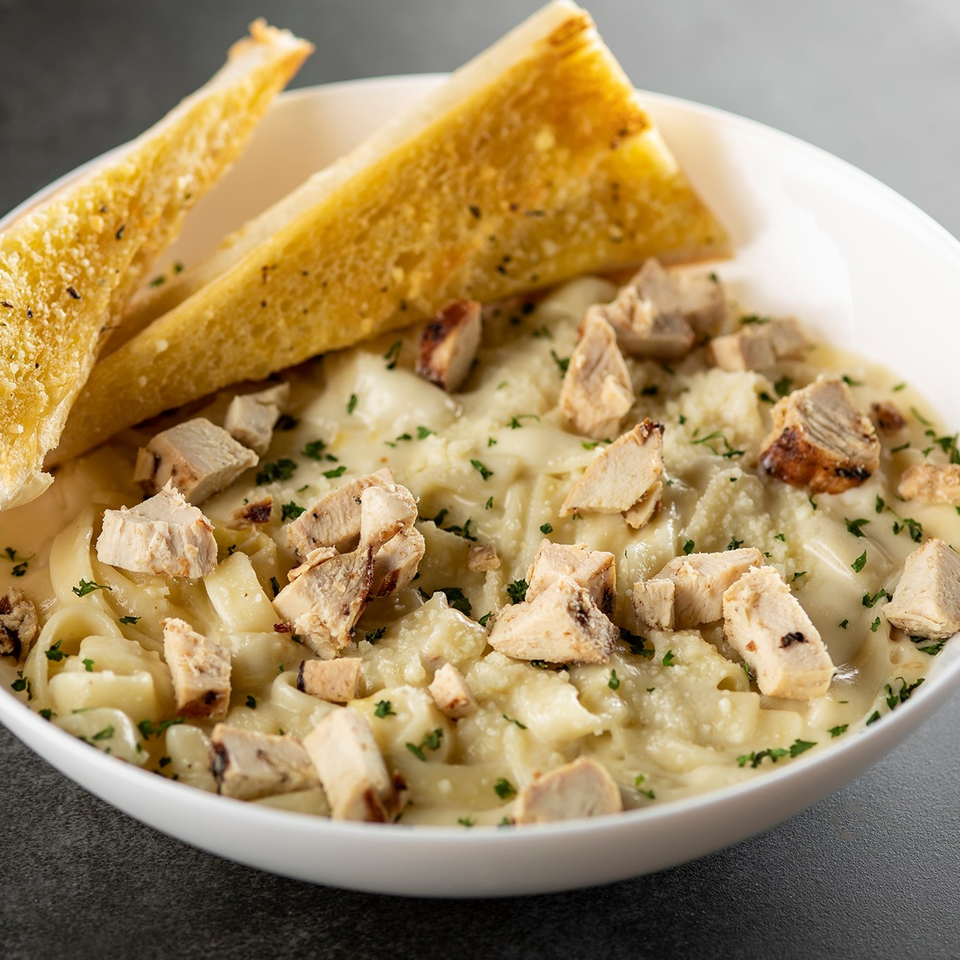 Creamy pasta with diced chicken, parmesan cheese, and parsley, served with two slices of garlic bread.