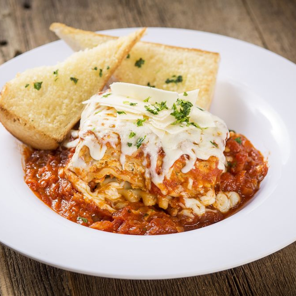 A serving of lasagna with melted cheese and tomato sauce, garnished with parsley, served with garlic bread.