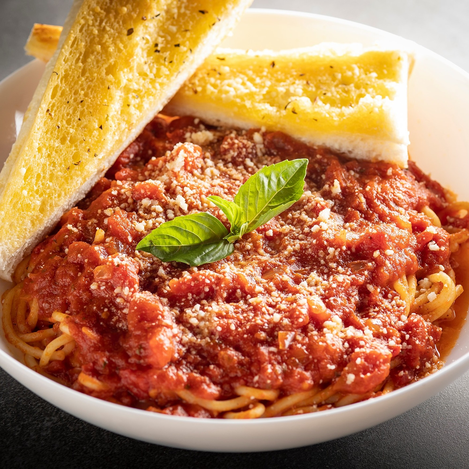 Spaghetti with rich red marinara sauce, grated cheese, fresh basil, and two slices of garlic bread.